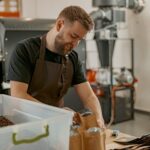 Business owner in uniform packs roasted coffee beans into packages for sale